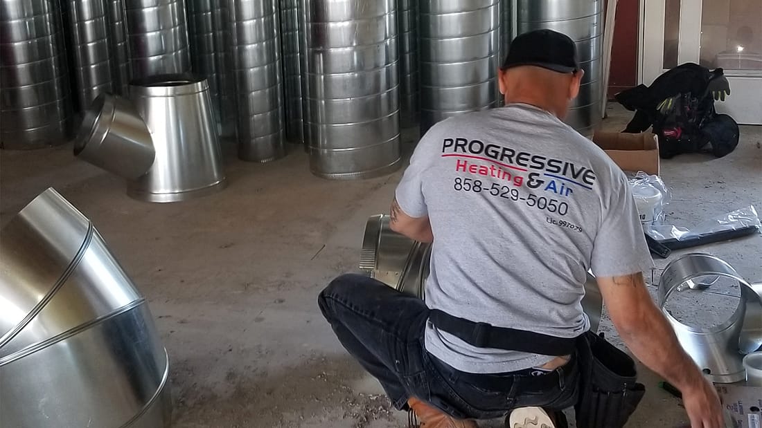 Progressive Heating & Air technician assembling ductwork on a San Diego job